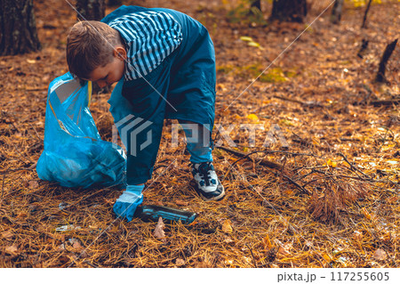 Cleaning the forest from garbage waste. A child with a garbage bag collects garbage in the forest. The problem of forest pollution with waste, an environmental disaster. Cleaning the forest from garbage waste. A child with a garbage bag collects garbage in the forest. The problem of forest pollution with waste, an environmental disaster. 117255605