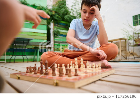 Boy concentrating on a chess game with his friend outdoors on a sunny day 117256196