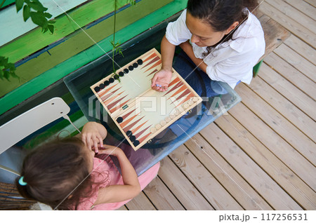 Mother and daughter playing backgammon at a table in an outdoor setting Mother and daughter playing backgammon at a table in an outdoor setting 117256531