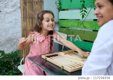 Mother and daughter enjoying a fun game of backgammon outdoors in a garden setting Mother and daughter enjoying a fun game of backgammon outdoors in a garden setting 117256556