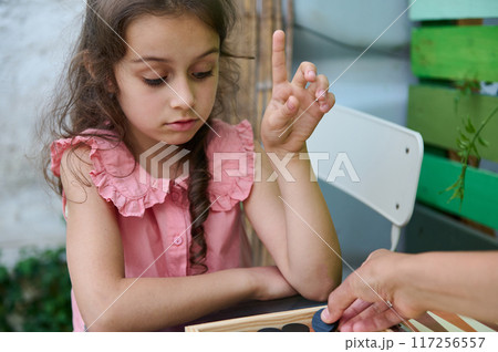 Young girl playing a board game with concentration and raising finger outdoors Young girl playing a board game with concentration and raising finger outdoors 117256557