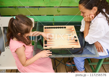 Mother and daughter playing backgammon while spending quality time together outdoors Mother and daughter playing backgammon while spending quality time together outdoors 117256576