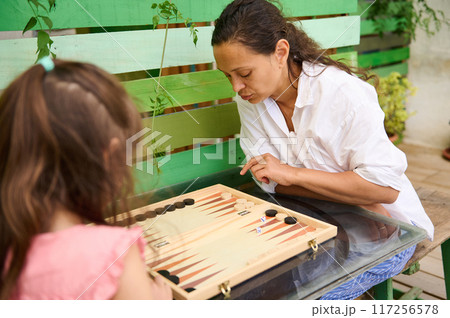 Mother and daughter playing backgammon together in a garden setting Mother and daughter playing backgammon together in a garden setting 117256578
