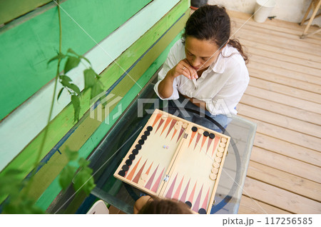 Woman playing backgammon outdoors on a wooden deck for a relaxing leisure activity Woman playing backgammon outdoors on a wooden deck for a relaxing leisure activity 117256585