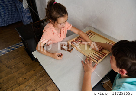Two children playing backgammon at home, enjoying a fun and strategic board game Two children playing backgammon at home, enjoying a fun and strategic board game 117258556
