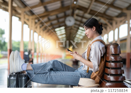 Young female traveler carrying a backpack waits for the train at the train station to travel alone. 117258834