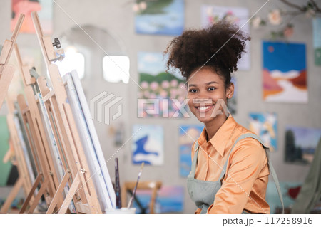 A young black artist paints acrylic paints on canvas with determination in her painting studio A young black artist paints acrylic paints on canvas with determination in her painting studio 117258916