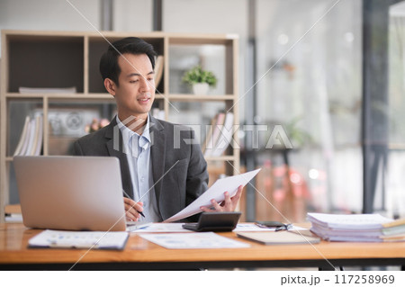 Young Asian businessman working using laptop in modern office, analyzing accounts Financial investment information report 117258969