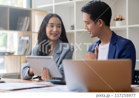 A young businessman and a female Asian accountant are discussing financial accounting and business planning together in the office. 117258977