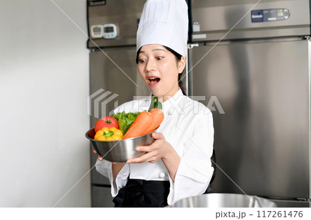 沢山の野菜を持ちながら驚く若い女性調理師 沢山の野菜を持ちながら驚く若い女性調理師 117261476