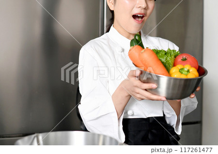 沢山の野菜を持ちながら驚く若い女性調理師 沢山の野菜を持ちながら驚く若い女性調理師 117261477