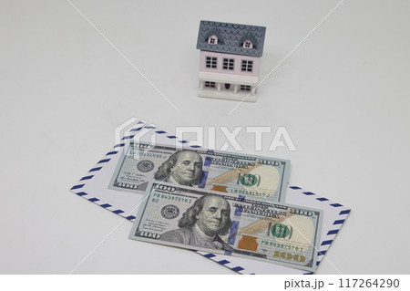 Banknotes in a white envelope and a toy house, funds for the purchase of real estate. Banknotes in a white envelope and a toy house, funds for the purchase of real estate. 117264290