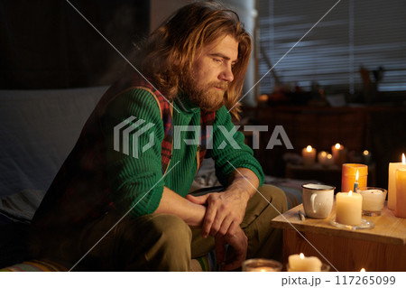 Man Sitting by Candlelight in Cozy Room Contemplating Life Man Sitting by Candlelight in Cozy Room Contemplating Life 117265099