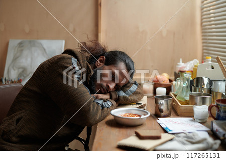 Sleeping Man Leaning on Table Surrounded by Objects 117265131