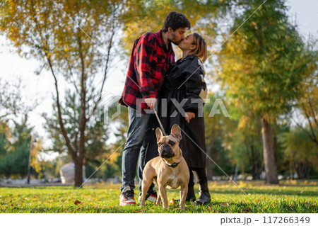 A couple shares a romantic moment with their dog in an autumn park. Beautiful scenery with fall colors A couple shares a romantic moment with their dog in an autumn park. Beautiful scenery with fall colors 117266349