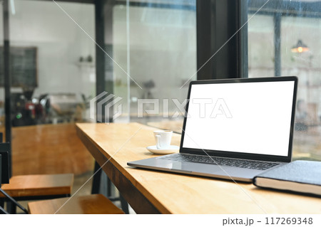 Laptop with blank screen, coffee cup and book on wooden table neat glass wall 117269348