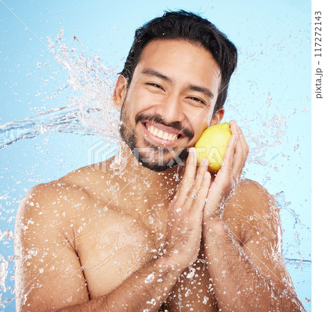 Skincare, water and portrait of man with a lemon in studio for healthy, organic and natural face routine. Health, wellness and man from India with citrus fruit for facial treatment by blue background 117272143