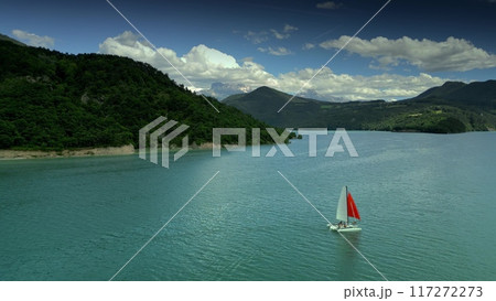 Aerial view of a sailboat or trimaran with the red sail on the Lake of Monteynard-Avignonet on French Alps background 117272273