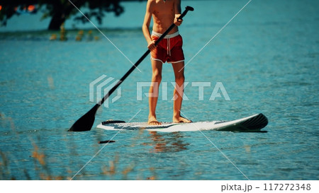 Unknown standing boy paddles a paddle board or SUP, summer vacation time 117272348