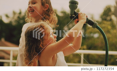 Little girls have fun with a water sprinkler hose on a hot summer day at home, slow motion Little girls have fun with a water sprinkler hose on a hot summer day at home, slow motion 117272354