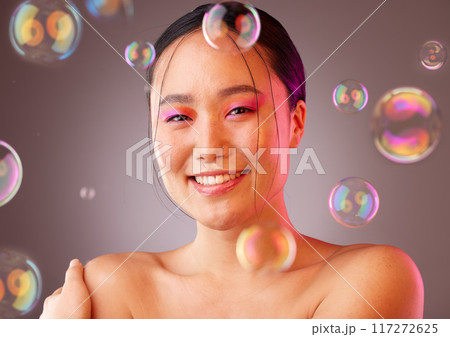 Makeup, bubbles and Asian woman with smile, for cosmetics, skincare or health on a studio background. Portrait of a young girl with body care, natural beauty or happiness for organic facial 117272625