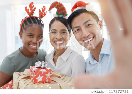 Office, friends and selfie with gift in christmas celebration at work, cheerful, smile and relax while having fun together. Diversity, party and colleagues gathering for festive photo and event 117272721