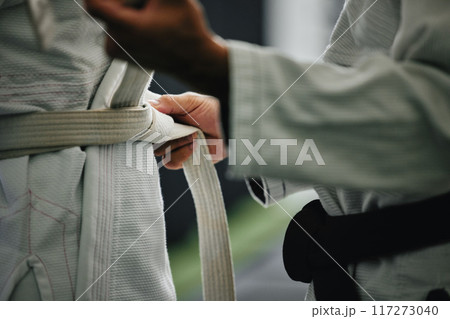 Karate learning, training and workout of a sport student and coach getting ready for a fight class. Defense expert hands tie a belt in a dojo, workout studio or wellness club about to work on fitness Karate learning, training and workout of a sport student and coach getting ready for a fight class. Defense expert hands tie a belt in a dojo, workout studio or wellness club about to work on fitness 117273040