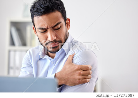 Bad muscle pain in the arm, shoulder and body after an injury and ache while working in the office. Angry, upset and frustrated businessman with a painful strain, hurt and sore sitting at his desk 117273087