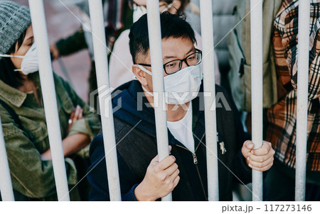 Sick, trapped young covid patient stuck in the city feeling like a prisoner, wearing a medical face mask. Foreign asian man in a crowd during a pandemic. Male following city healthcare safety rules. 117273146