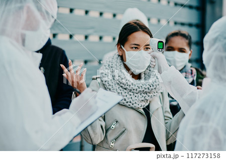 Health care worker scanning a frustrated woman temperature for corona with a thermometer. Concerned female made victim of racial profiling, looking annoyed and angry during the pandemic Health care worker scanning a frustrated woman temperature for corona with a thermometer. Concerned female made victim of racial profiling, looking annoyed and angry during the pandemic 117273158