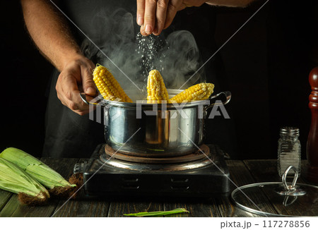 The chef adds salt to a pot of hot corn cobs. The concept of making delicious maize in a restaurant kitchen. A unique recipe for making maize 117278856