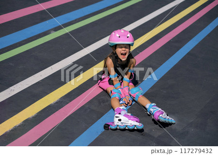 A hysterical girl screams while sitting on the track of a roller rink after falling from roller skates 117279432