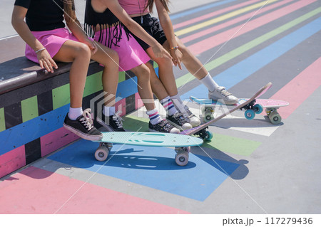 Three Girls are sitting on a skatepark bench with skates, close-up Three Girls are sitting on a skatepark bench with skates, close-up 117279436