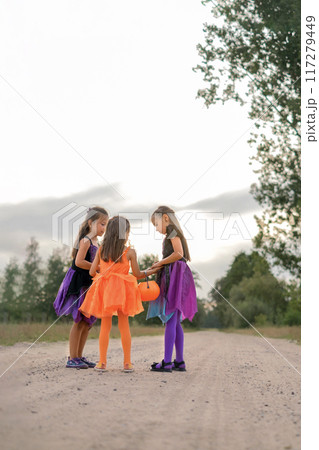 Girls in Halloween witch costumes are chatting in the middle of a sandy street with a bucket in the shape of a pumpkin 117279449