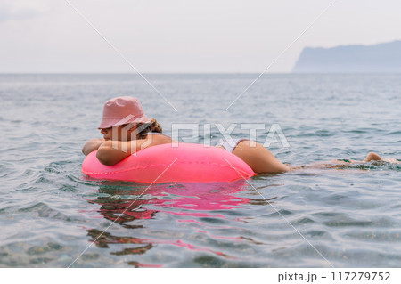 A woman is laying on a pink inflatable raft in the ocean. The scene is peaceful and relaxing, with the woman enjoying the water and the sun. 117279752