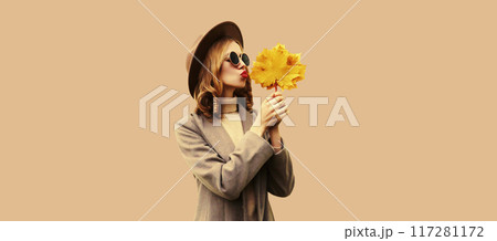 Autumn color style outfit, beautiful young woman with yellow maple leaves wearing round hat, coat 117281172