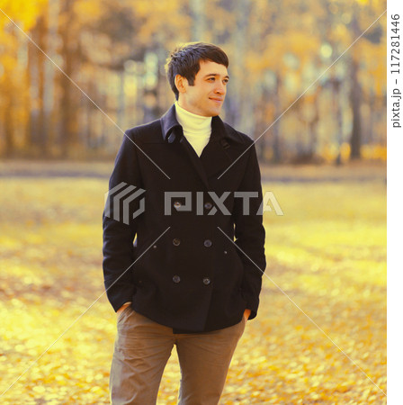 Portrait of elegant caucasian young man in black coat outdoors in autumn park with yellow leaves 117281446