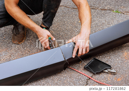 When aluminum rain gutters have been bent on machine tool, worker cuts them to required size with shears 117281862