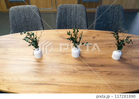 Three vases with greenery placed on a wooden table in an indoor setting 117281890