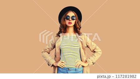 Portrait of beautiful woman posing wearing black round hat, coat jacket on brown studio background Portrait of beautiful woman posing wearing black round hat, coat jacket on brown studio background 117281982