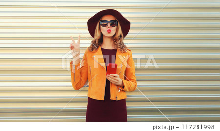 Portrait of stylish young woman posing blowing her lips sends sweet air kiss holds phone 117281998
