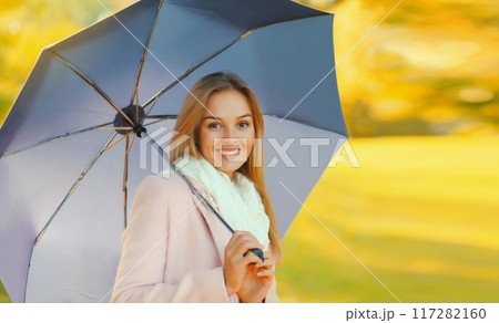 Portrait of beautiful happy smiling blonde young woman with umbrella in sunny autumn park 117282160
