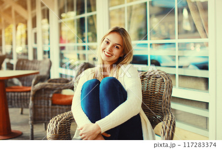 Portrait of beautiful blonde smiling young woman sitting on chair waiting in city cafe Portrait of beautiful blonde smiling young woman sitting on chair waiting in city cafe 117283374