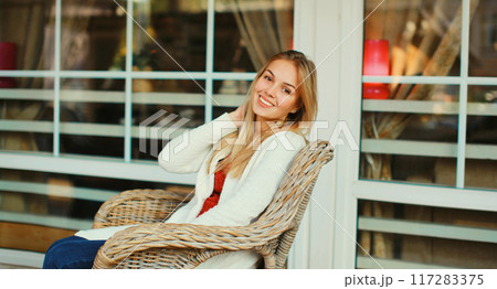 Portrait of beautiful blonde smiling young woman sitting on chair waiting in city cafe Portrait of beautiful blonde smiling young woman sitting on chair waiting in city cafe 117283375