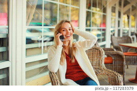 beautiful blonde smiling young woman calling on mobile phone sitting on chair waiting in city cafe beautiful blonde smiling young woman calling on mobile phone sitting on chair waiting in city cafe 117283379