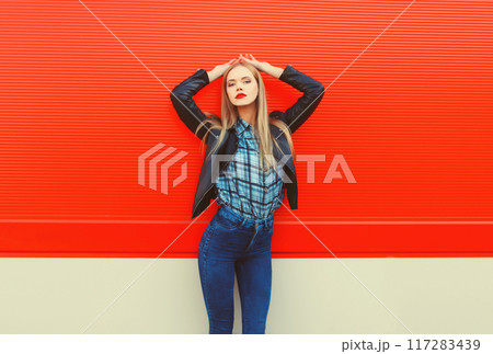 Fashion portrait of beautiful blonde young woman posing in black leather jacket on red background Fashion portrait of beautiful blonde young woman posing in black leather jacket on red background 117283439