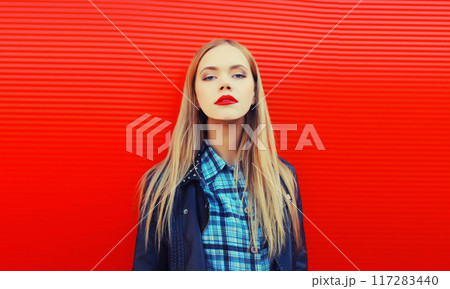 Fashion portrait of beautiful blonde young woman posing in black leather jacket on red background Fashion portrait of beautiful blonde young woman posing in black leather jacket on red background 117283440