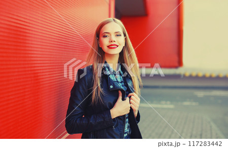 Fashion portrait of beautiful blonde young woman posing in black leather jacket on red background Fashion portrait of beautiful blonde young woman posing in black leather jacket on red background 117283442