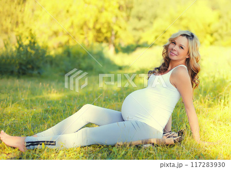 Happy young pregnant woman resting sitting on the grass in summer park 117283930
