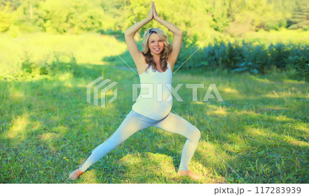 Happy young pregnant woman doing yoga training on the grass in summer park 117283939